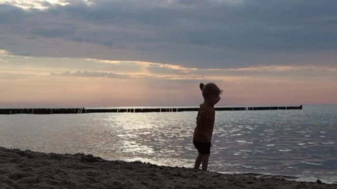 一个小男孩自信地沿着沙子走到海边，并在日落时分将石头扔进水中