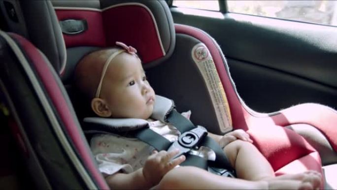担心的亚洲女婴坐在汽车座椅上旅行。婴儿第一次体验长途汽车旅行或公路旅行概念。亚洲法律加强在车辆中使用