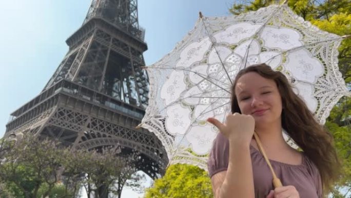 巴黎美丽的年轻少女在埃菲尔铁塔的背景下，穿着浪漫主义风格的优雅长裙，带着一把雨伞从阳光下行走，微笑着