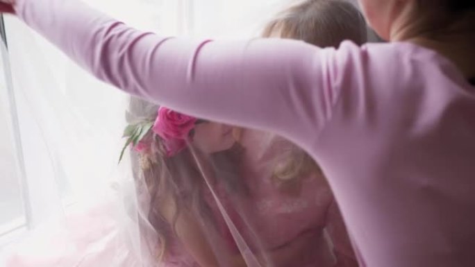 后台摄影师与美丽的家庭母亲和女儿在大窗户附近的粉红色连衣裙