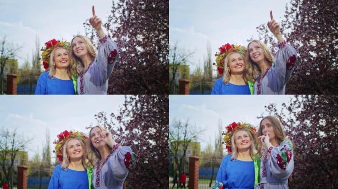 两个快乐的女人头上戴着花环，在盛开的粉红色樱花花的背景下欢欣鼓舞。周末日落时带着微笑漫步。女人和春天