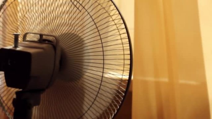 夏天，一个带炉排的旧风扇在一个带窗帘的房间里转动并冷却空气