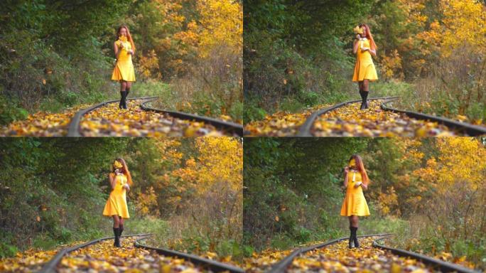 一个红头发的女孩，在黄色和橙色的叶子之间的秋天森林里。红发女人在泛黄的树木中沿着一条自然的铁路行走。