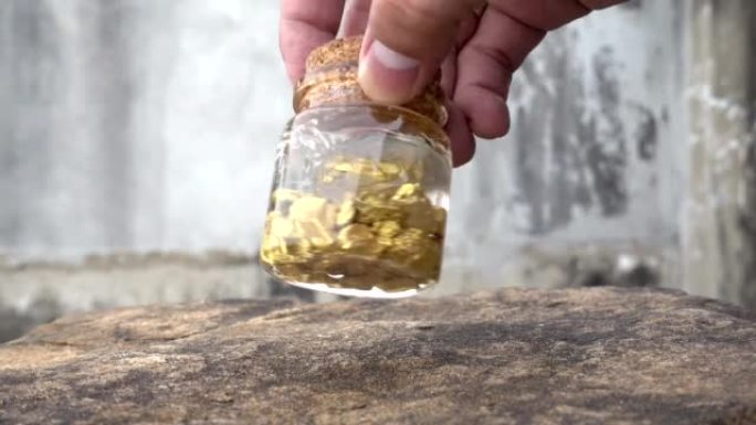 人的手在摇摆着装有矿山中发现的纯金矿物质的瓶子。