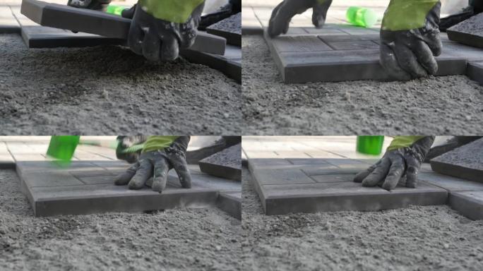 建筑商的双手戴着工作手套，将铺路石放在均匀的沙子上，并用沉重的塑料锤敲打瓷砖。慢动作，细节