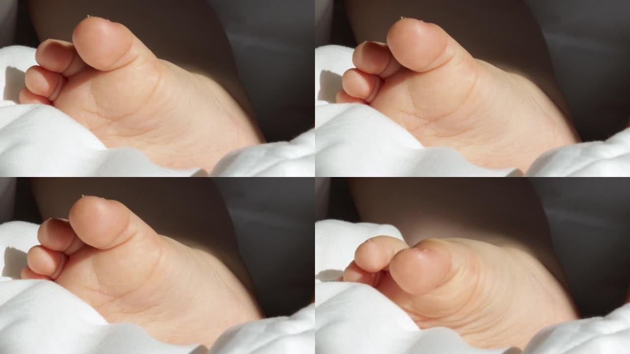 婴儿可爱的小脚在白色毯子上，阳光明媚的光线落在蹒跚学步的腿上。男婴入睡，轻柔的手指移动，爱心关怀家庭