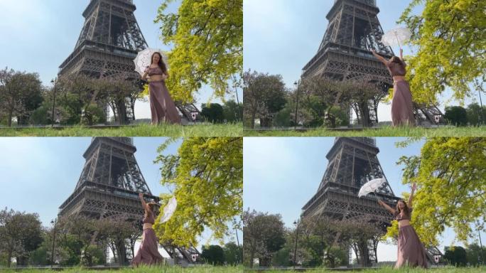 巴黎美丽的年轻少女在埃菲尔铁塔的背景下，穿着长长的别致的连衣裙微笑着跳舞
看着镜头，她留着长长的金发