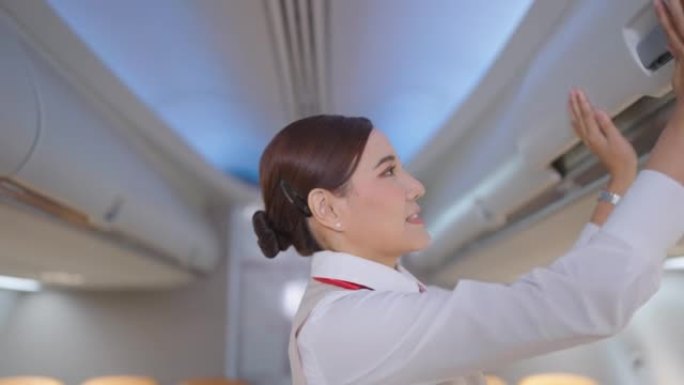 穿着制服的亚洲空姐乘务员走在过道上关闭行李舱，并在起飞前与乘客交谈，检查飞机的准备情况。