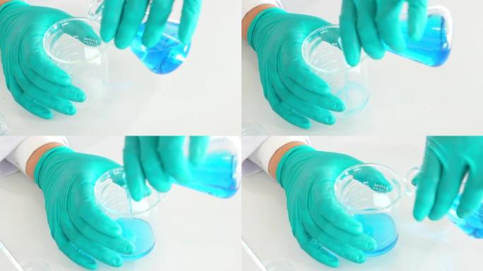 专业化学家的特写手穿着防护制服，戴着手套，将移液器中的溶液加入到烧瓶中的蓝色混合物中。在现代实验室工