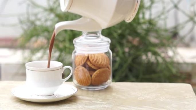 茶壶在茶杯和茶碟中倒茶，背景为饼干