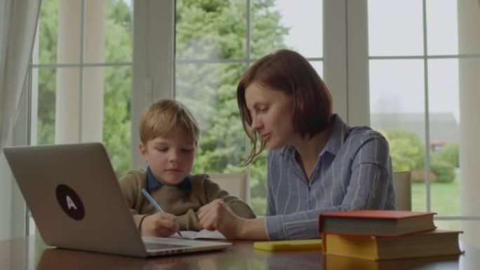 30多岁的年轻母亲在家和学校的孩子做在线作业。家庭使用笔记本电脑一起学习。在线教育过程。