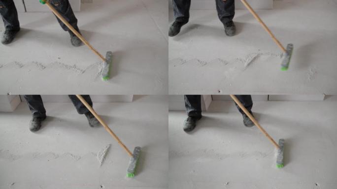 一名工人修理后刷地板。一名工人从地板上扫除白色混凝土灰尘。在家维修工作后的垃圾收集。