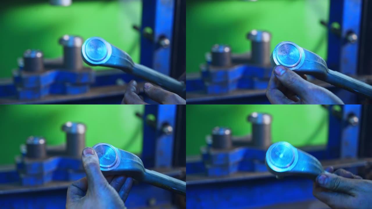 特纳正在拍摄一个金属细节，并用手指检查。模糊背景下的金属工具和机器。