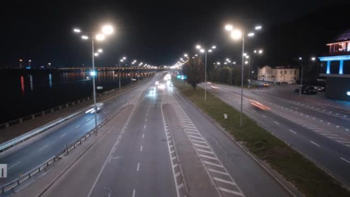 从长时间暴露的顶视桥上拍摄的城市道路的夜间过度。行驶前大灯的汽车在长轨道上行驶