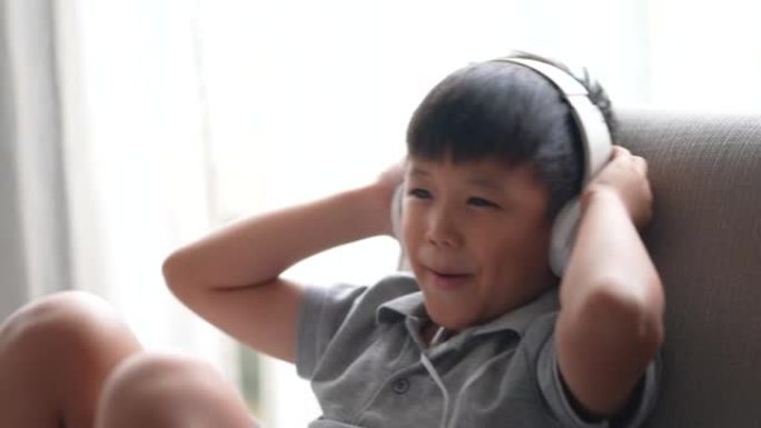 亚洲男孩在沙发上用耳机愉快地听音乐