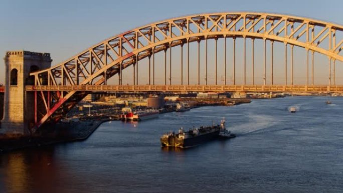 一艘驳船在纽约，长岛市，皇后区的地狱门桥下的东河上行驶，在停泊船只的商业文件前。航空无人机制作的带静