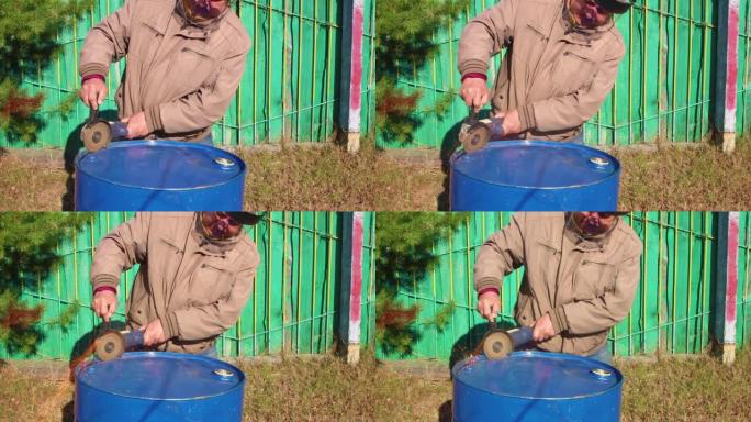 一名男子正在用角磨机切割蓝色金属桶。