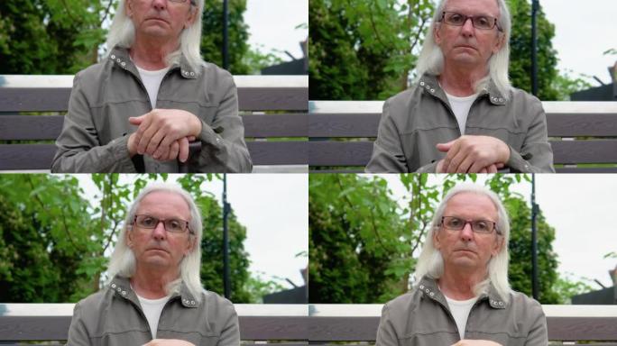 公共城市公园长凳上老人的肖像。快乐的老人看着相机。老年人在休闲时间玩得开心