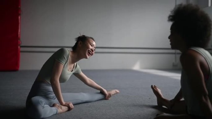 穿着瑜伽服的中国女人在健身房和朋友聊天，一边伸展身体