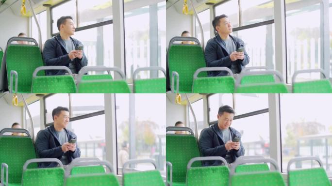 亚洲男子乘坐公共交通工具，坐在座位上使用手机，智能手机在公交车窗前。城市背景上的男性休闲肖像