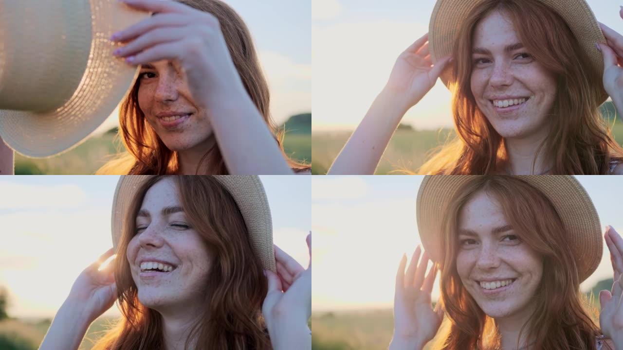 穿着夏装的雀斑开朗的红头发女孩在日落时戴上草帽戴在头上。美丽的姜女人在户外嬉戏地微笑。美丽的自然，风