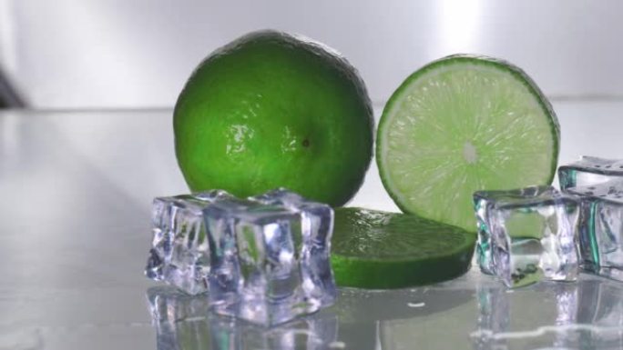 绿色柠檬是空白的，有一个切块，显示了柑橘皮的内部。透明玻璃反射柠檬和湿水的阴影，使其清新，冰增加冷却