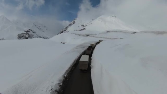 格鲁吉亚古达里美丽雪山的鸟瞰图。卡车车队沿着山路行驶