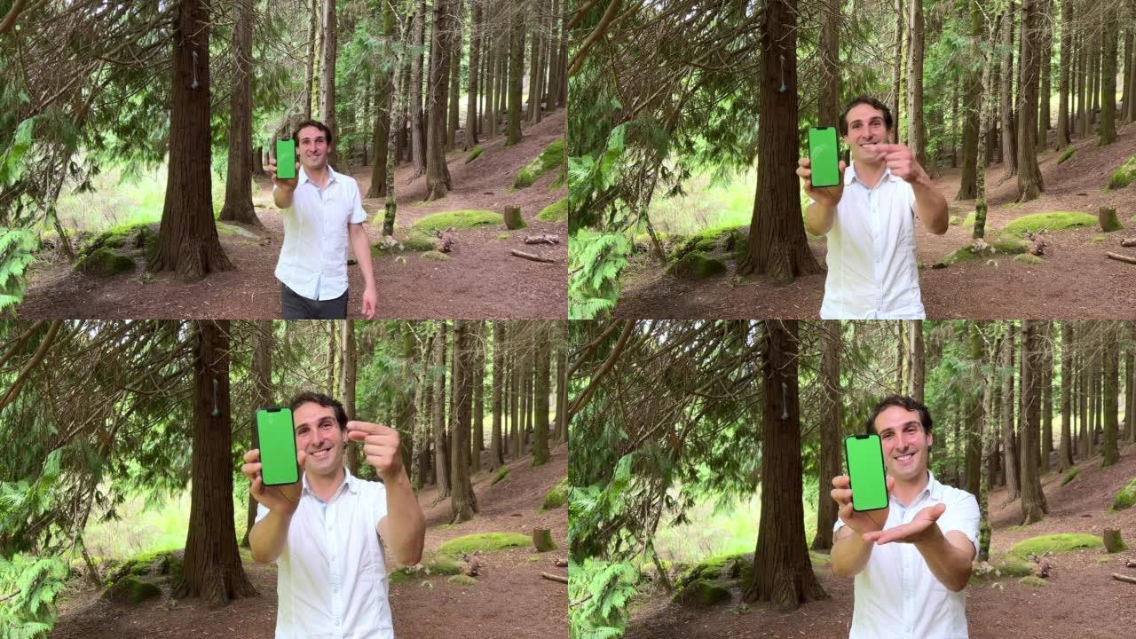 英俊的法国人拿着一部绿屏的手机，一瘸一拐地说，他穿着一件白衬衫，背景森林里有一头黑发，可以用来宣传科