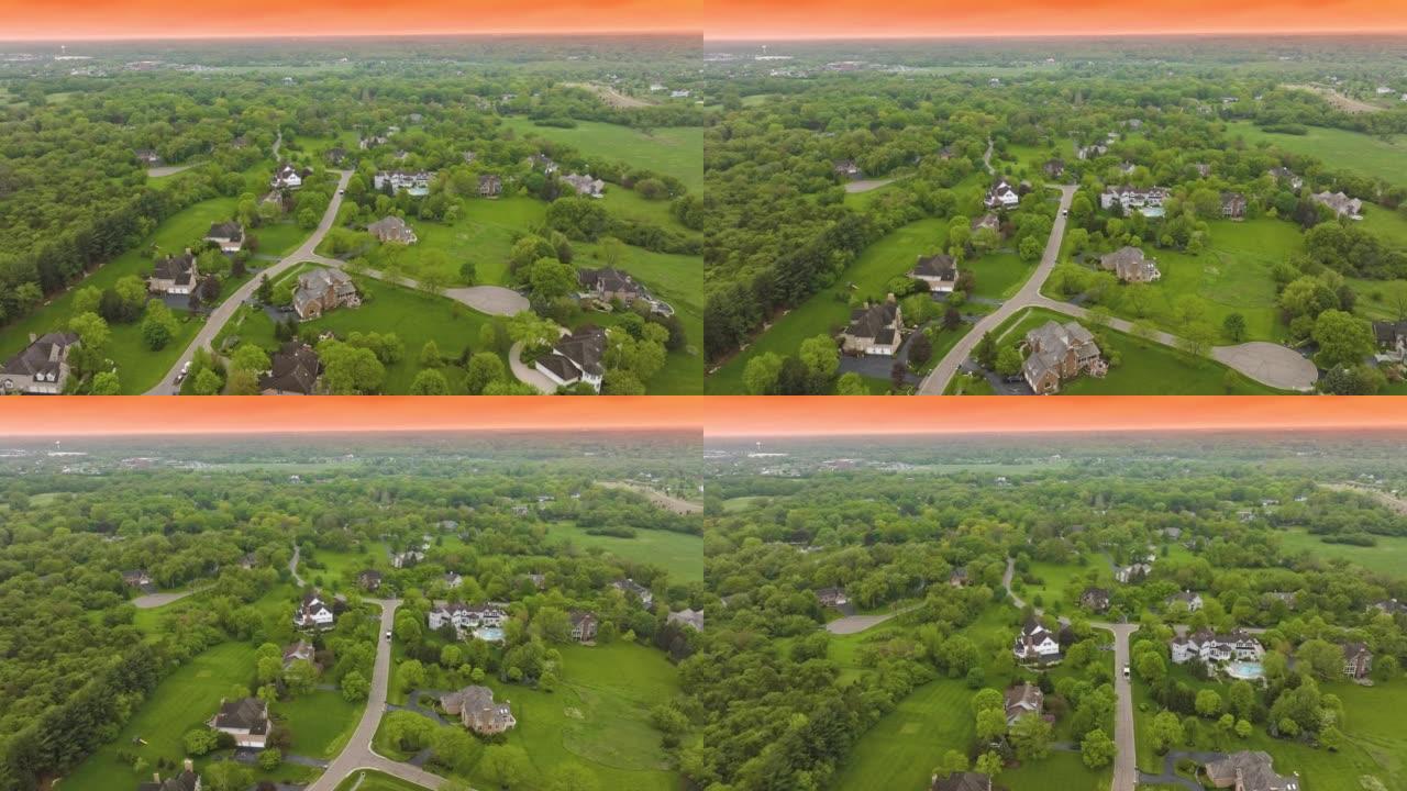 美国郊区保存完好，有美丽的私人住宅和整洁的道路。在橙色天空的背景下，被绿树和草地草坪包围的农村社区。