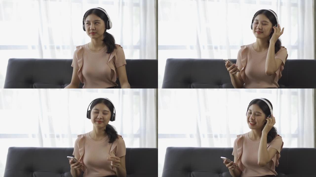 亚洲妇女戴着耳机在家里的沙发上用智能手机听音乐