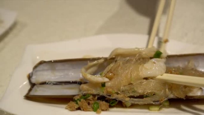 在中餐餐厅用筷子吃烤剃刀平静的玻璃面条