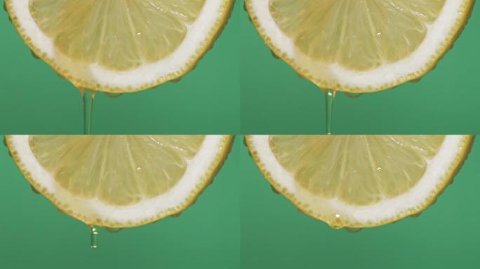 半柠檬片的慢动作微距拍摄，绿色屏幕背景上从柠檬中掉落的软聚焦粘性蜂蜜滴。
