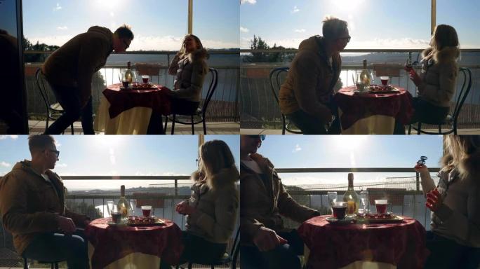 深情的年轻夫妇享受周末在舒适的乡村餐厅共度时光，湖面美景，微笑的夫妇坐在阳台的圆桌旁，热气腾腾的水果