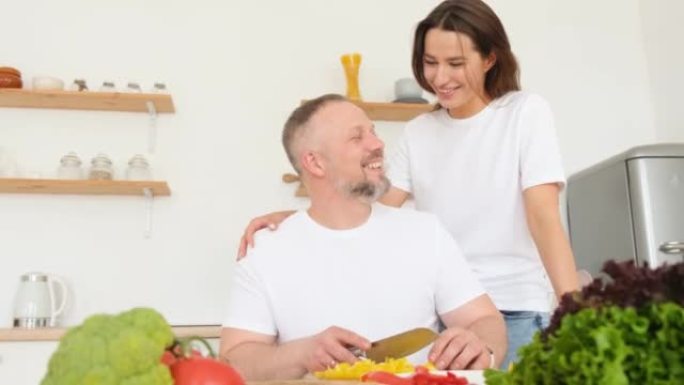 有爱心的女人拥抱一个准备晚餐的男人，家人在厨房里。这个人正在准备晚餐