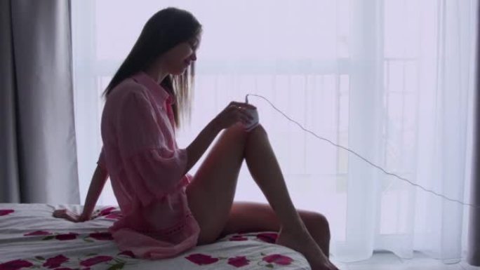 年轻女子在家里的腿上使用电子脱毛器。一个女人在家让自己脱毛。