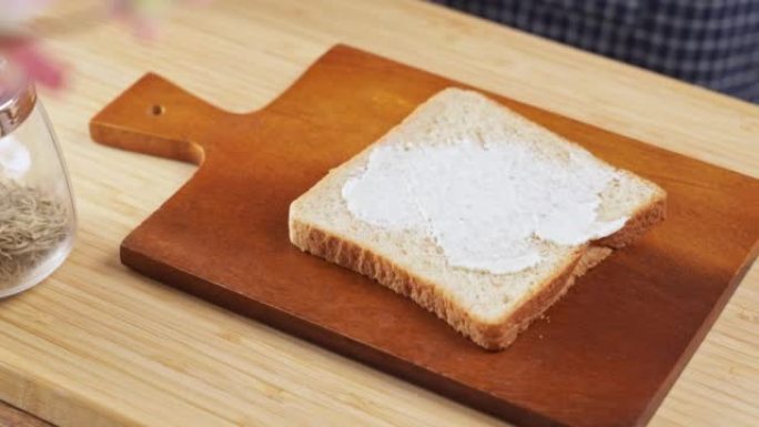 4k视频，涂抹在面包片上的奶油干酪。软奶油铺在酸面团面包上。女人用刀将奶油干酪铺在一块新鲜面包上。脂