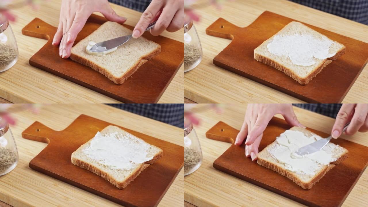 4k视频，涂抹在面包片上的奶油干酪。软奶油铺在酸面团面包上。女人用刀将奶油干酪铺在一块新鲜面包上。脂