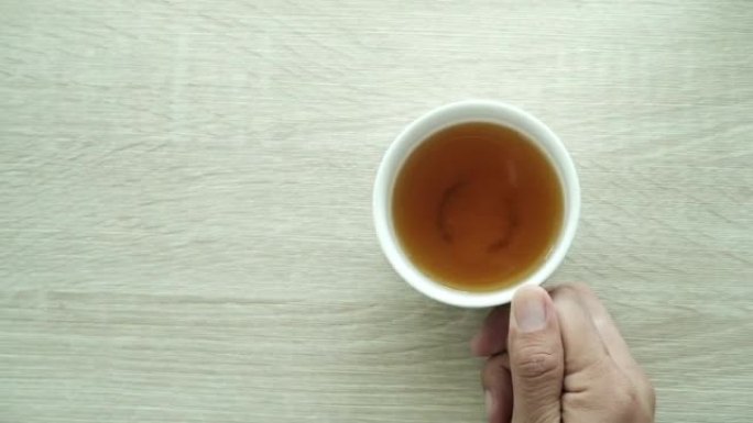 一个人的手在浅棕色的木桌上的白色茶杯中冲泡绿茶。俯视图，慢动作