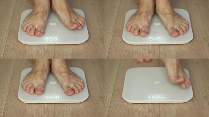 步行男性检查BMI体重减轻。人体赤脚测量身体脂肪超重。男人的腿踩在浴室秤上。减肥人的脚站在房间里称重