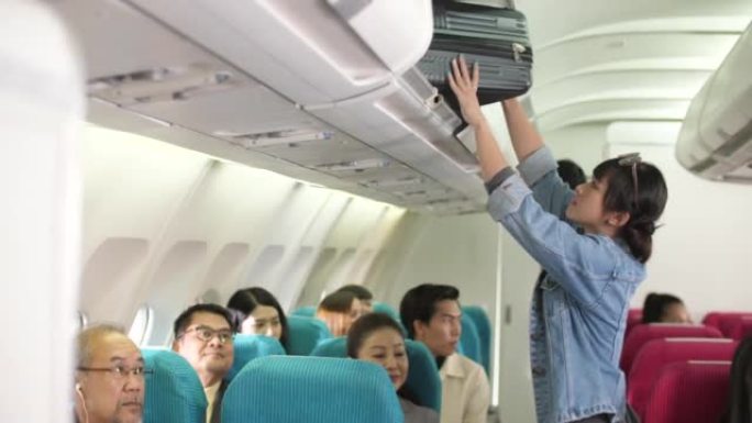 飞机乘务员帮助乘客将行李放在高架行李箱中