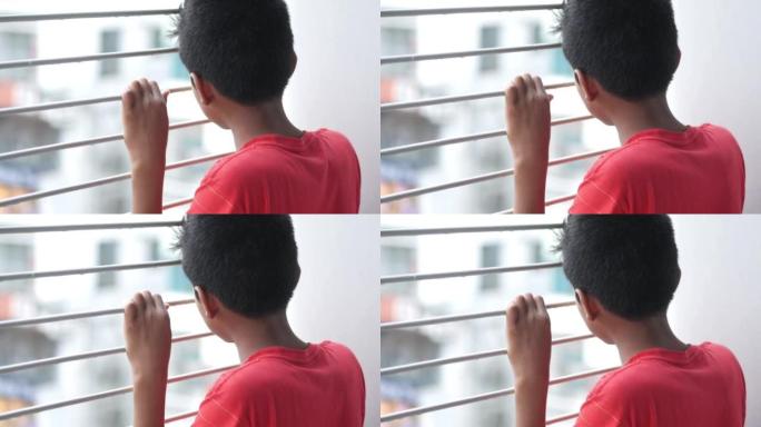 悲伤的十几岁的男孩透过窗户看