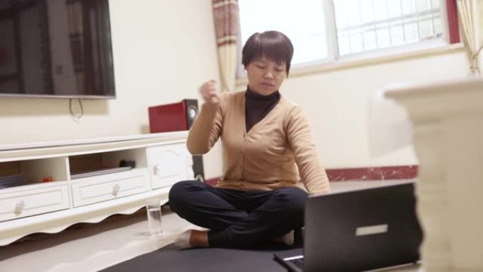 一名中年妇女在瑜伽垫上使用笔记本电脑学习健身方式-技术和生活，健康的生活方式