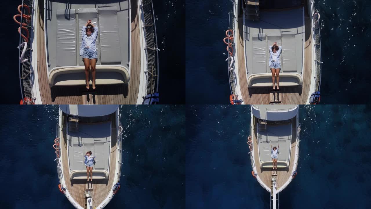 年轻漂亮的女人在游艇甲板上晒日光浴会发出空气亲吻和挥手