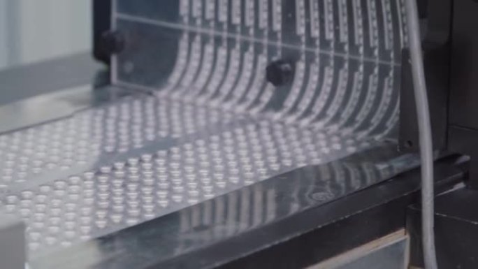自动机器将药丸包装到泡罩容器中的特写镜头。塑料包装的药片在传送带上移动。化工厂生产过程中的装配线。