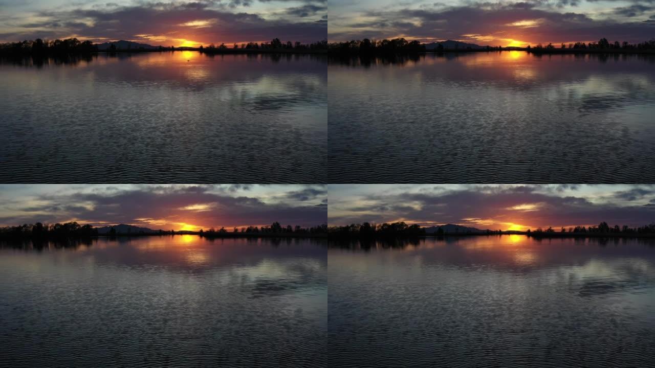 日落时的湖泊，阴天的日落反射在水面上，一条鱼跳出水面