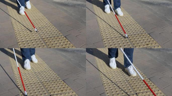 盲人的腿用手杖寻找特殊的触觉瓷砖。盲人拄着拐杖在街上行走