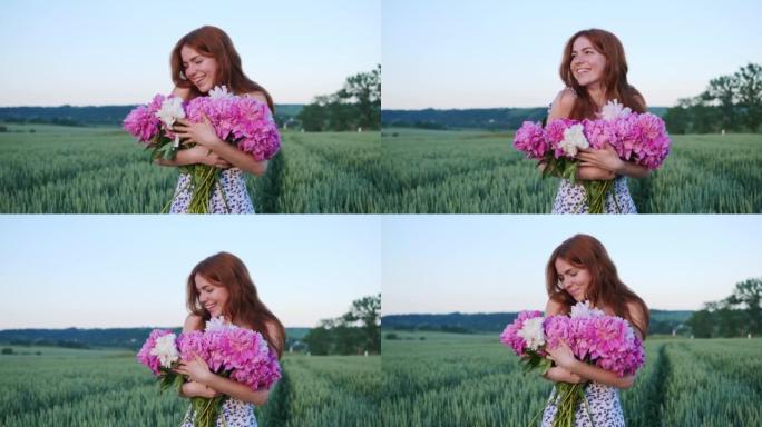 快乐美丽的红发年轻姜黄色雀斑女孩。女人拿着粉红色的花朵牡丹看起来享受自由日落户外绿色麦田背景下迷人的