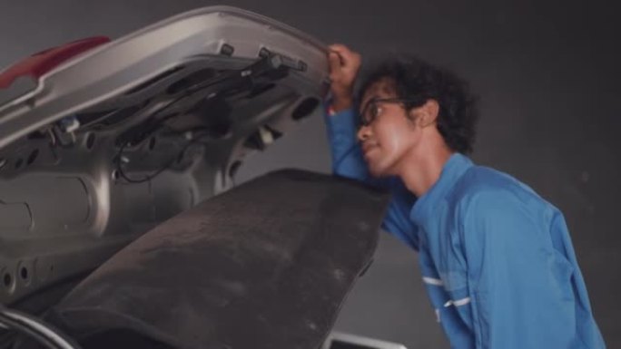 穿着蓝色机械连身衣的亚洲中年汽车工程师打开汽车行李箱，用于检查连接到后视摄像头的电缆