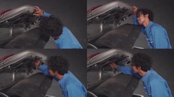 穿着蓝色机械连身衣的亚洲中年汽车工程师打开汽车行李箱，用于检查连接到后视摄像头的电缆