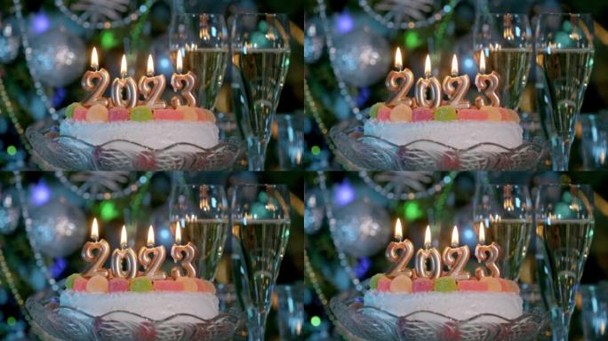 圣诞香槟和圣诞蛋糕装饰着燃烧的蜡烛在圣诞节和新年假期的背景。两杯起泡的起泡饮料。新年快乐2023